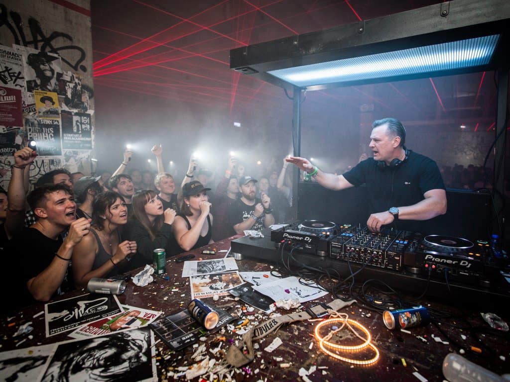 Berlin nightclub with Music Millennium AI Backlash cancelled poster, glitchy waveforms, empty DJ booth and protest outside in electronic music scene